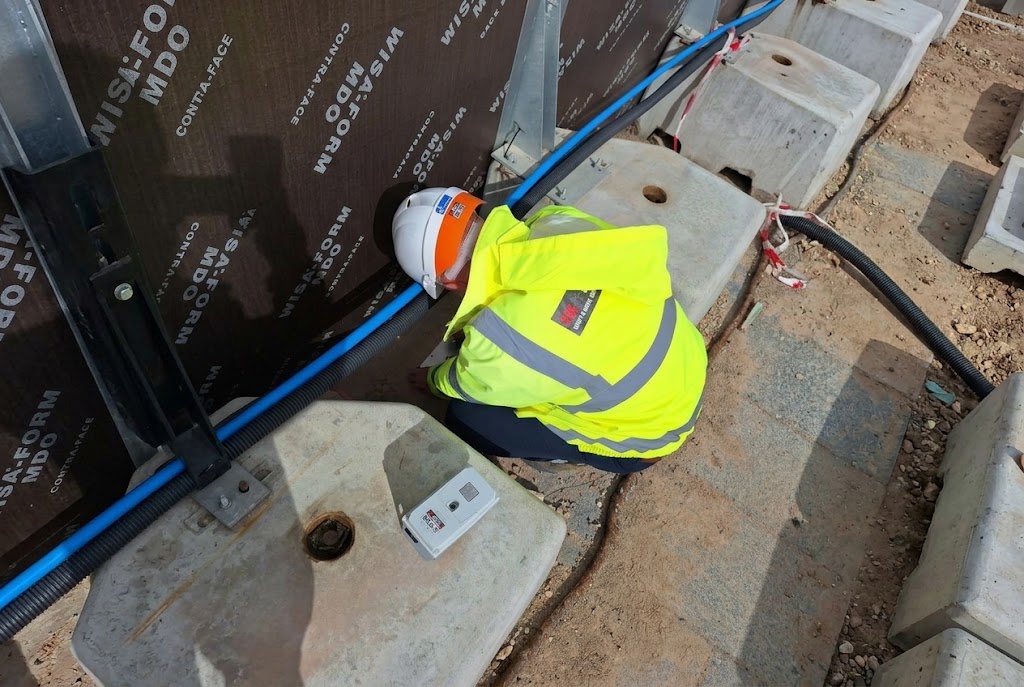 PQS Survey site technician installing a vibration monitor on a construction site next to formwork panels.